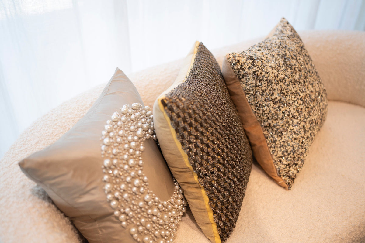 Three hand-beaded throw pillows in pearl, bronze and gold on an ivory boucle sofa
